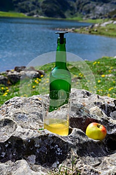 Green bottle and glass of natural Asturian cider made fromÂ fermented apples with view on Covadonga lake and tops of Picos de